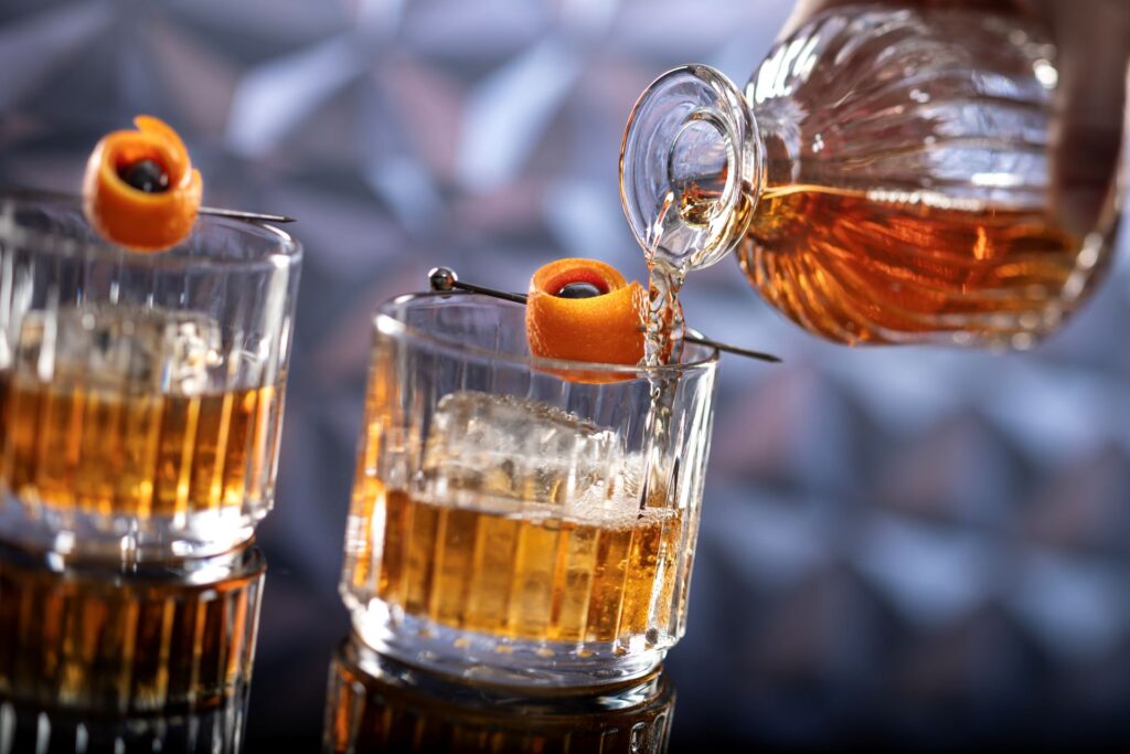 Bourbon is poured into tumble glasses garnished with an orange peel